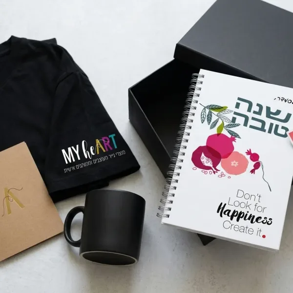צילום Flat lay של ערכת קבלת פנים מסודרת על שולחן: מחברת ממותגת, ספל, חולצה עם לוגו וכרטיס ברכה.
